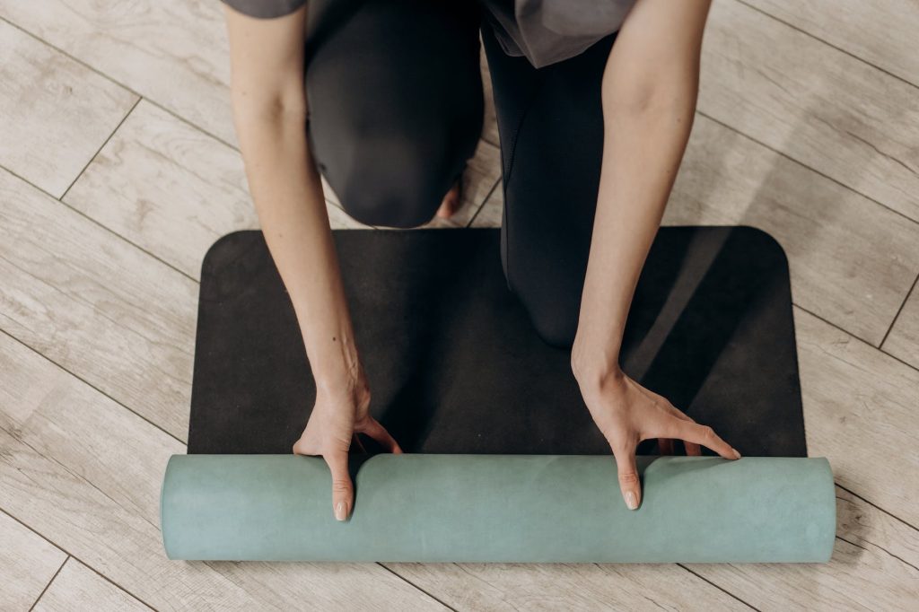 woman in black leggings unrolling a yoga mat - Infinity Online Consultations